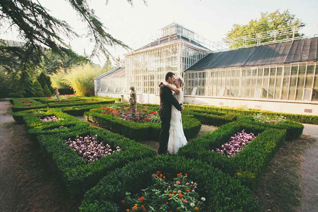 Nevesta in ženin se poljubljata sredi parka pred steklenim rastlinjakom. Foto: Alen Karupovič Photography