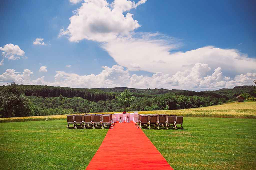Intimna postavitev civilnega poročnega obreda na posestvu Pule z rdečo preprogo, rdečimi vrtnicami in lesenimi stoli. Foto: Aperturia weddings