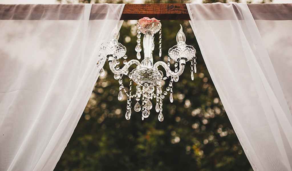 Prekrasen steklen 5 kraki lestenec visi na lesenem oboku med civilno poroko na prostem. Foto: Aleks & Irena Kus Wedding Photography
