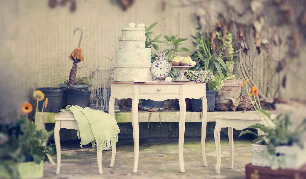 Bela tronadstropna poročna torta ter sladice na prekrasni starinski mizi, postavljeni ob bok dveh manjših mizic s cvetlično dekoracijo. Foto: arhiv Storija weddings