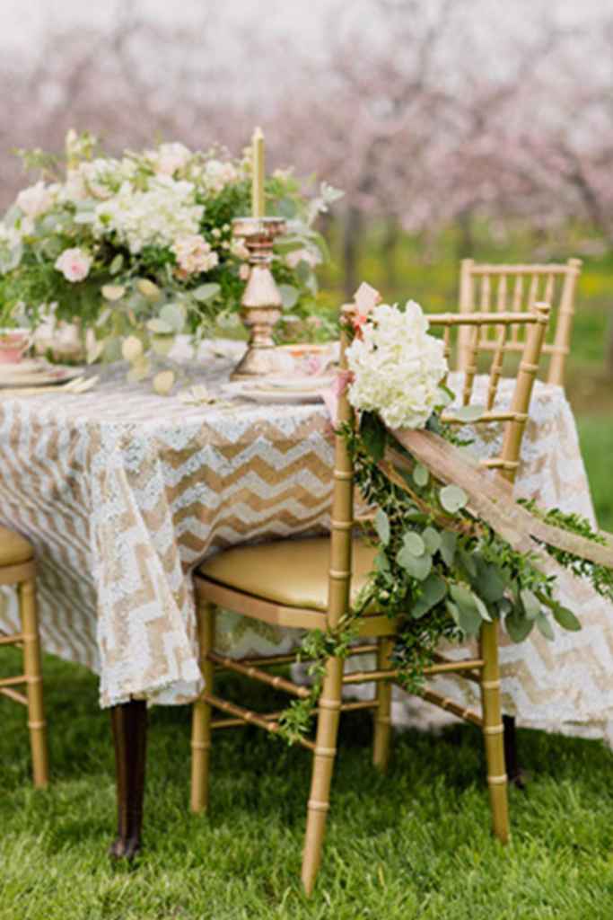 Cikcak prt s prepletom zelene in pastelne rumene barve je popestril poročno omizje. Na prtu so zlati svečniki in ležeč cvetlični aranžma v zeleno-rumenih odtenkih. Foto: Simply Lace Photography