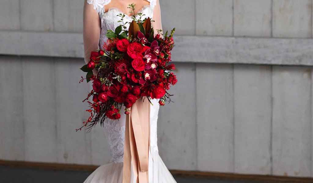 Nevesta v prekrasni elegantni beli poročni obleki v rokah drži velik rdeč poročni šopek, ki je resnično dih jemajoč. Foto: Visual Cravings