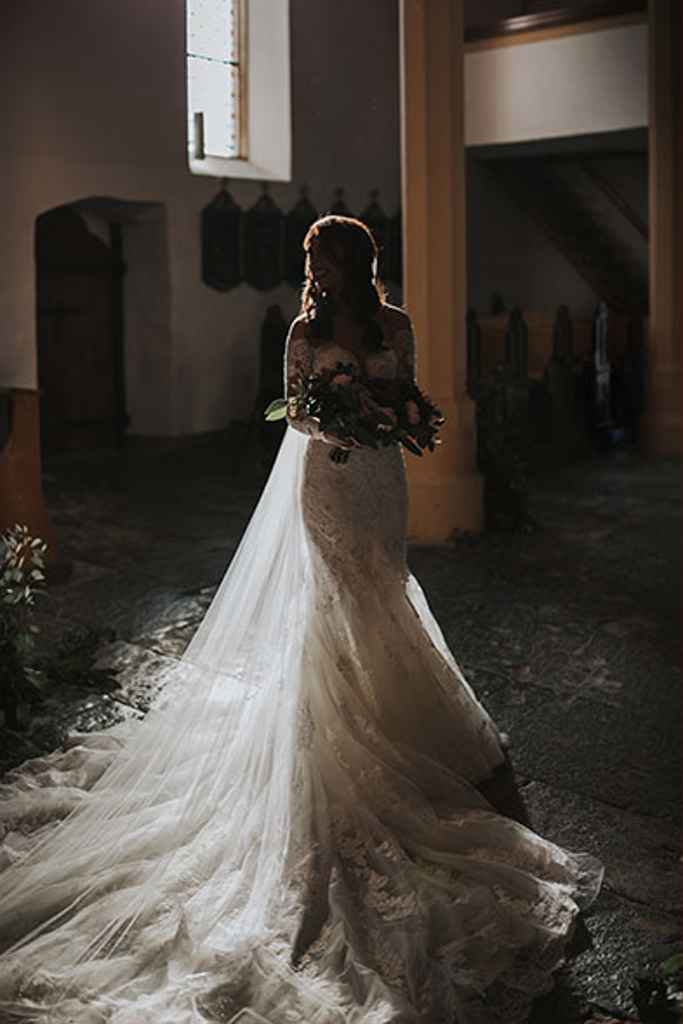 Petra Starbek stoji v cerkvi v svoji poročni obleki iz poročnega salona Sanjska obleka. Foto: Ana Gregorič Photography
