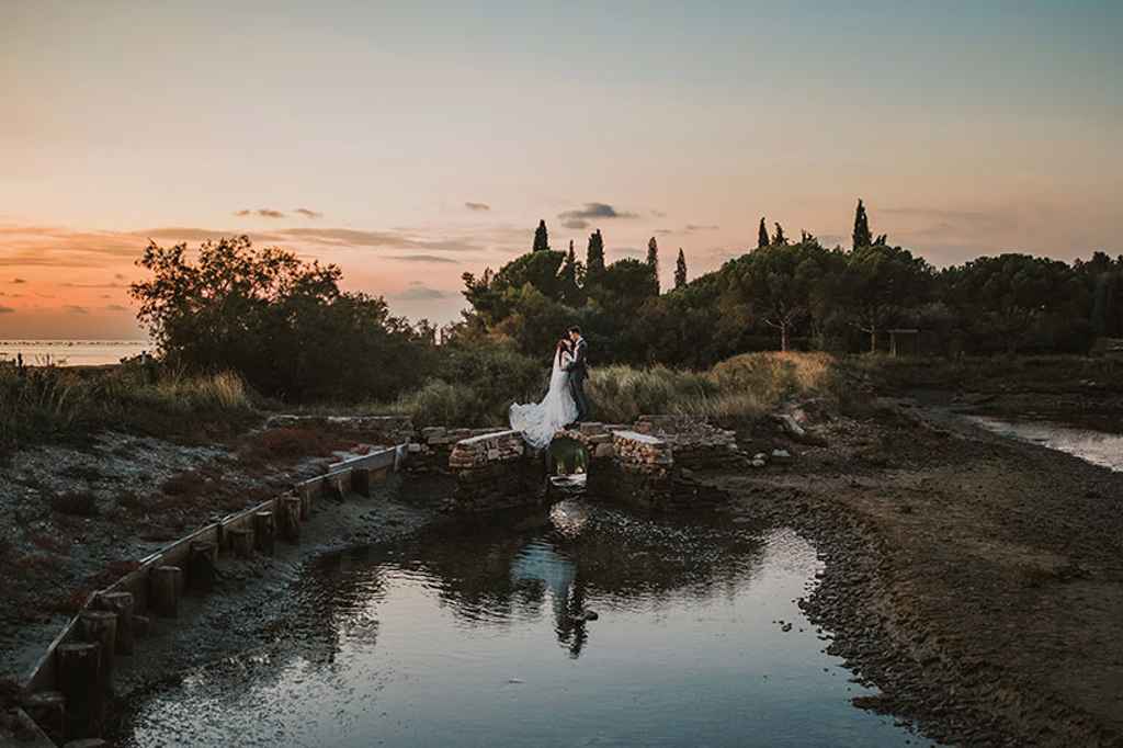 Mladoporočenca stojita na majhnem mostu in se poljubljata. Foto: Ana Gregorič Photography