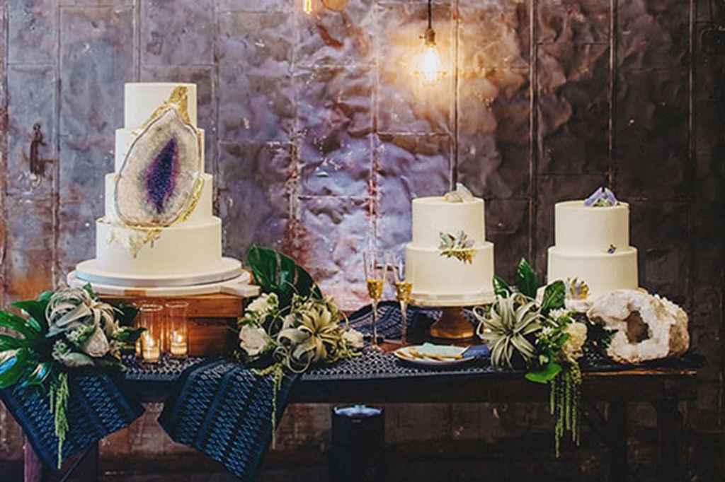 Tri poročne torte v belo vijola poročni tematiki. Prva je tronadstropna in v videzu dragega vijola kamna na beli torti, drugi sve sta dvonadstropni in z vijola poslikavi. Foto: Twopair photography