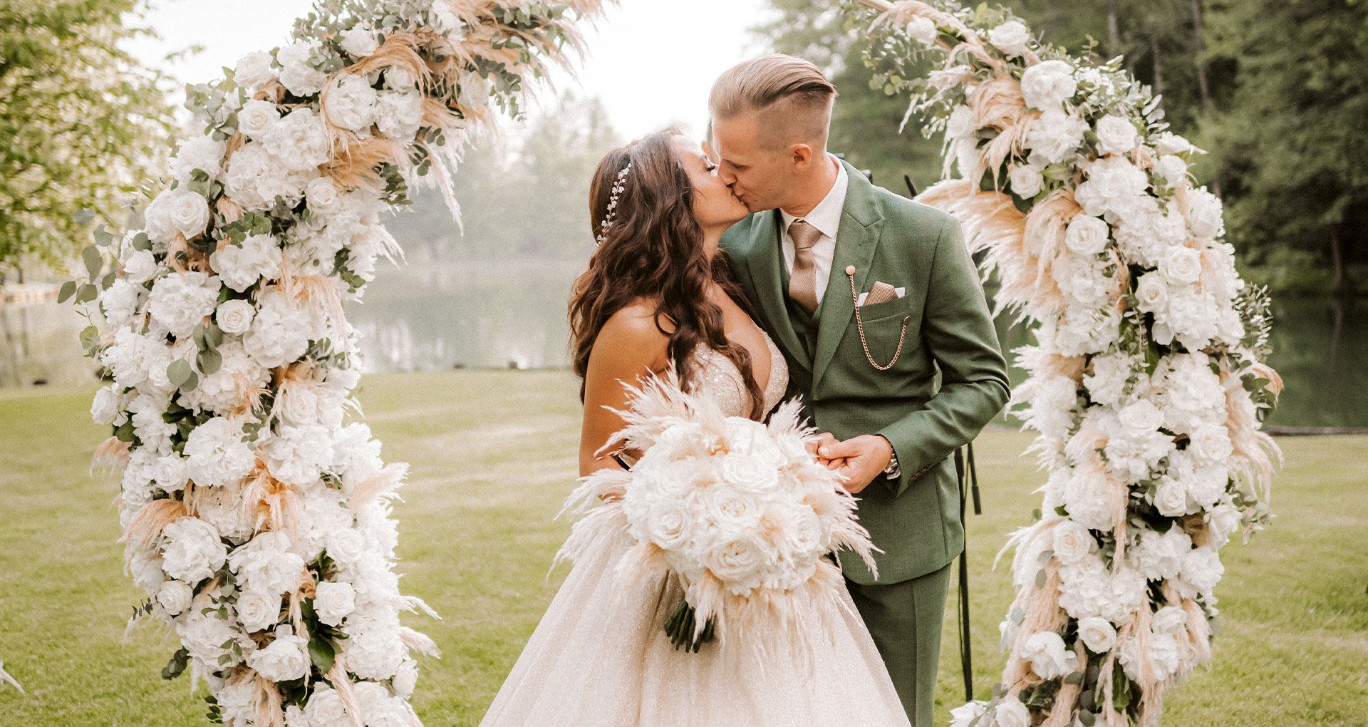 Organizacija porok - ženin in nevesta se poljubljata pod čudovitim cvetličnim obokom na posestvu Brdo pri Kranju.