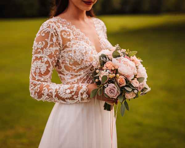 Nevesta drži v rokah prekrasen romantičen poročni šopek v pastelnih barvah s potonikami, evkaliptusom ter drugim cvetjem, ki ga je pripravila Polona iz cvetličarne Omers.